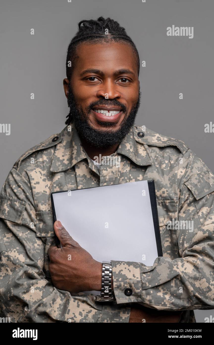 Porträt eines freudigen Soldaten, der mit einem leeren Blatt Papier an der Brust auf das Klemmbrett drückt. Stockfoto