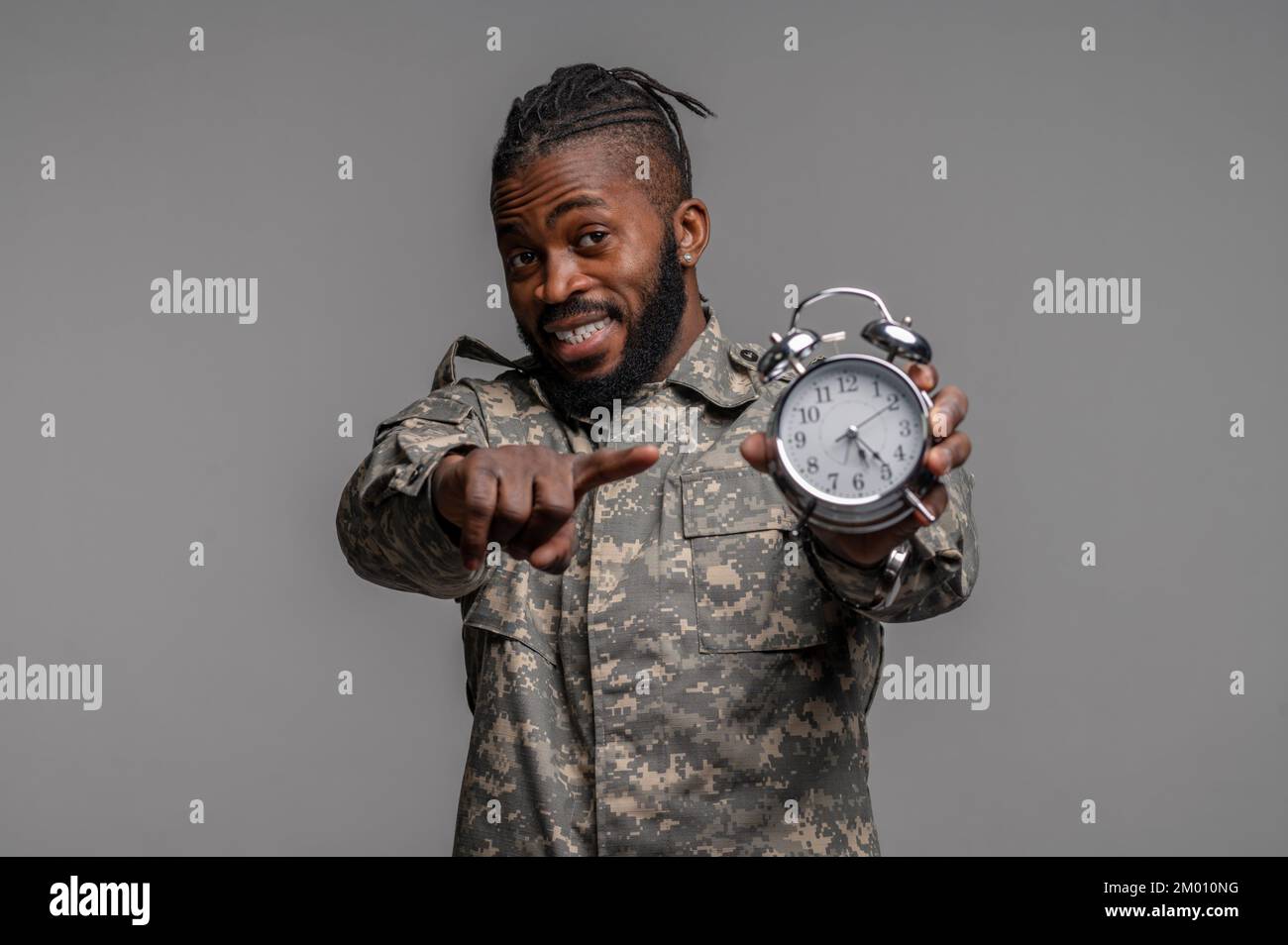 Hüftporträt eines jungen Soldaten, der eine Uhr hält und mit dem Zeigefinger nach vorne zeigt. Stockfoto