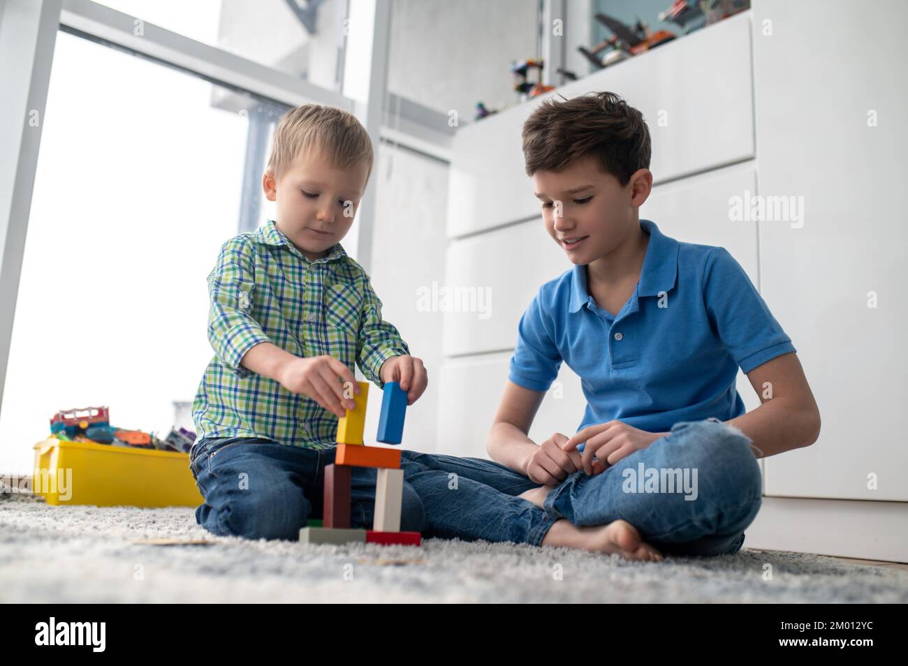 Ruhiges, konzentriertes Kind, das kleine Bausteine aus Plastik in Gegenwart seines älteren Bruders zusammenfügt. Stockfoto