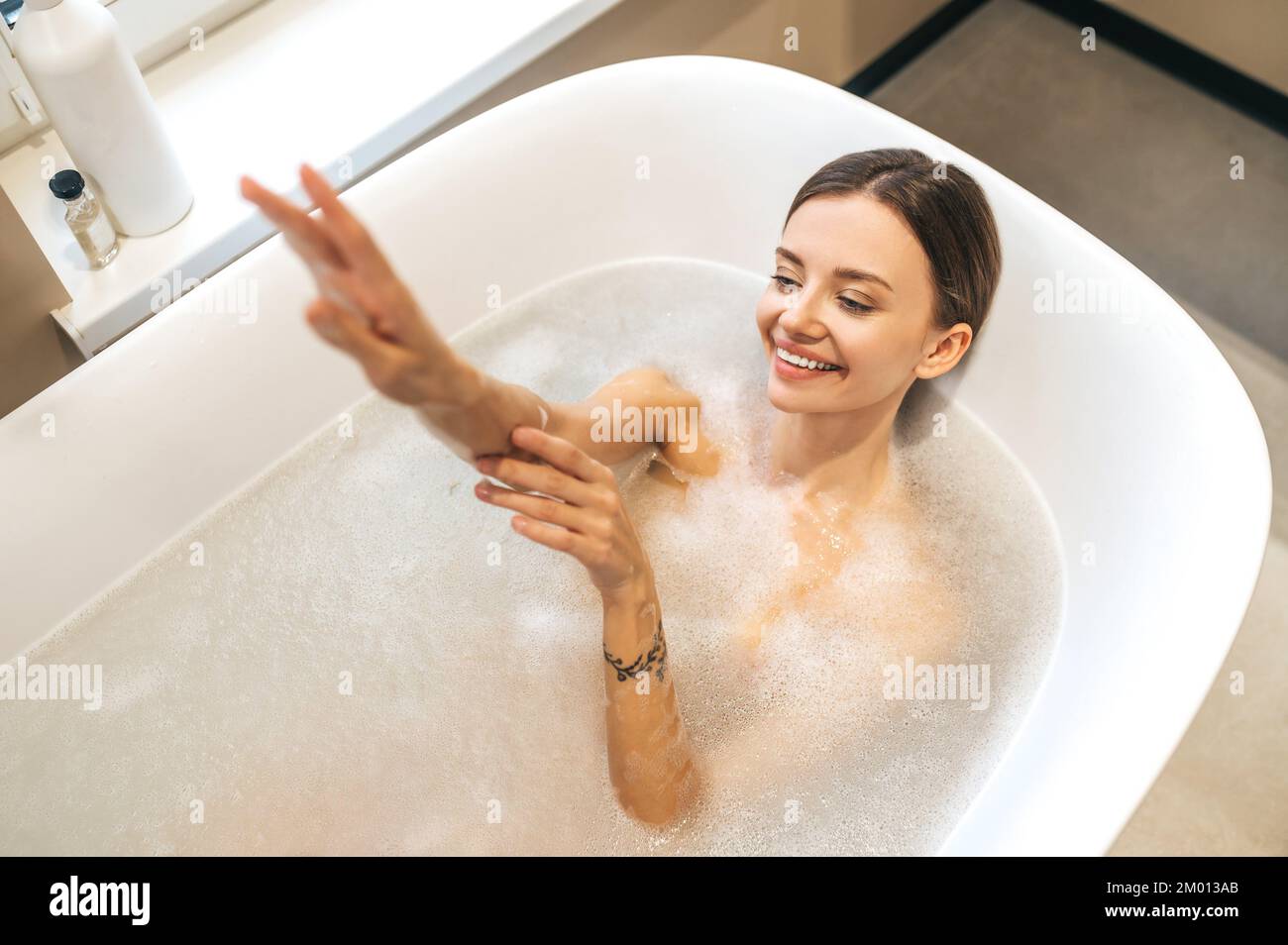 Top Aussicht auf eine lächelnde, wunderschöne Frau, die in der Badewanne lag, gefüllt mit Seifenwasser. Stockfoto
