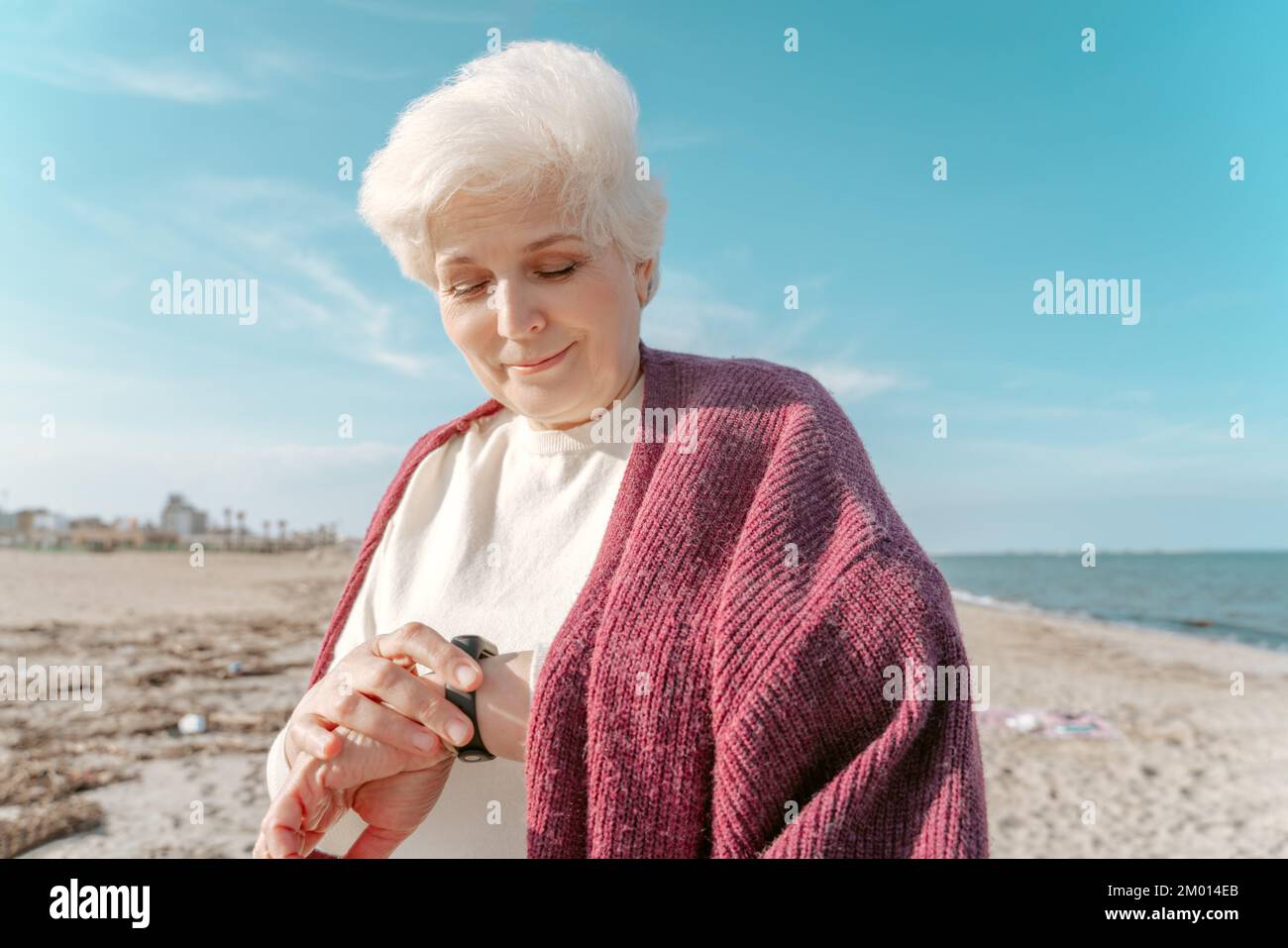 Hüftporträt einer lächelnden, zufriedenen Seniorin, die den Fitness-Tracker an ihrem Handgelenk ansieht. Stockfoto