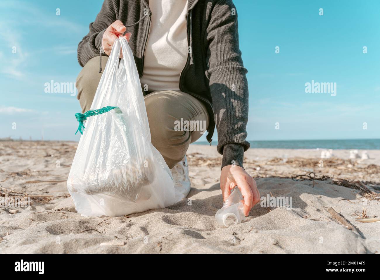 Abgeschnittenes Foto eines Umweltaktivisten, der eine weggeworfene Plastikflasche aus dem Sand holt. Stockfoto