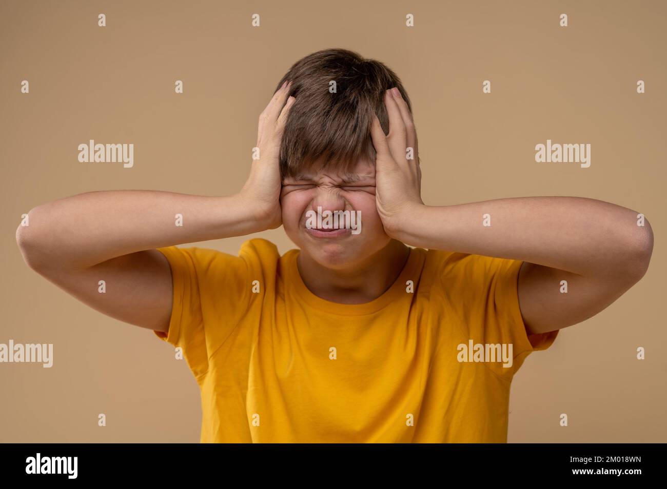 Porträt eines Teenagers mit geschlossenen Augen, der sich während der Migräneattacke mit beiden Händen an den Kopf klammert. Stockfoto