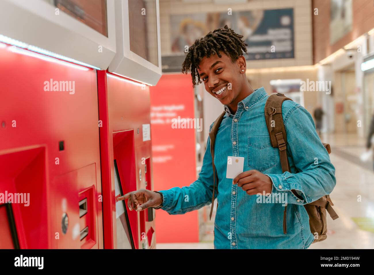 Guter Versuch. Ein afrikanischer Kerl, der vor der Kamera lächelt und zeigt, wie er ein Ticket gekauft hat, indem er das Selbstbedienungsterminal am Bahnhof berührt. Stockfoto