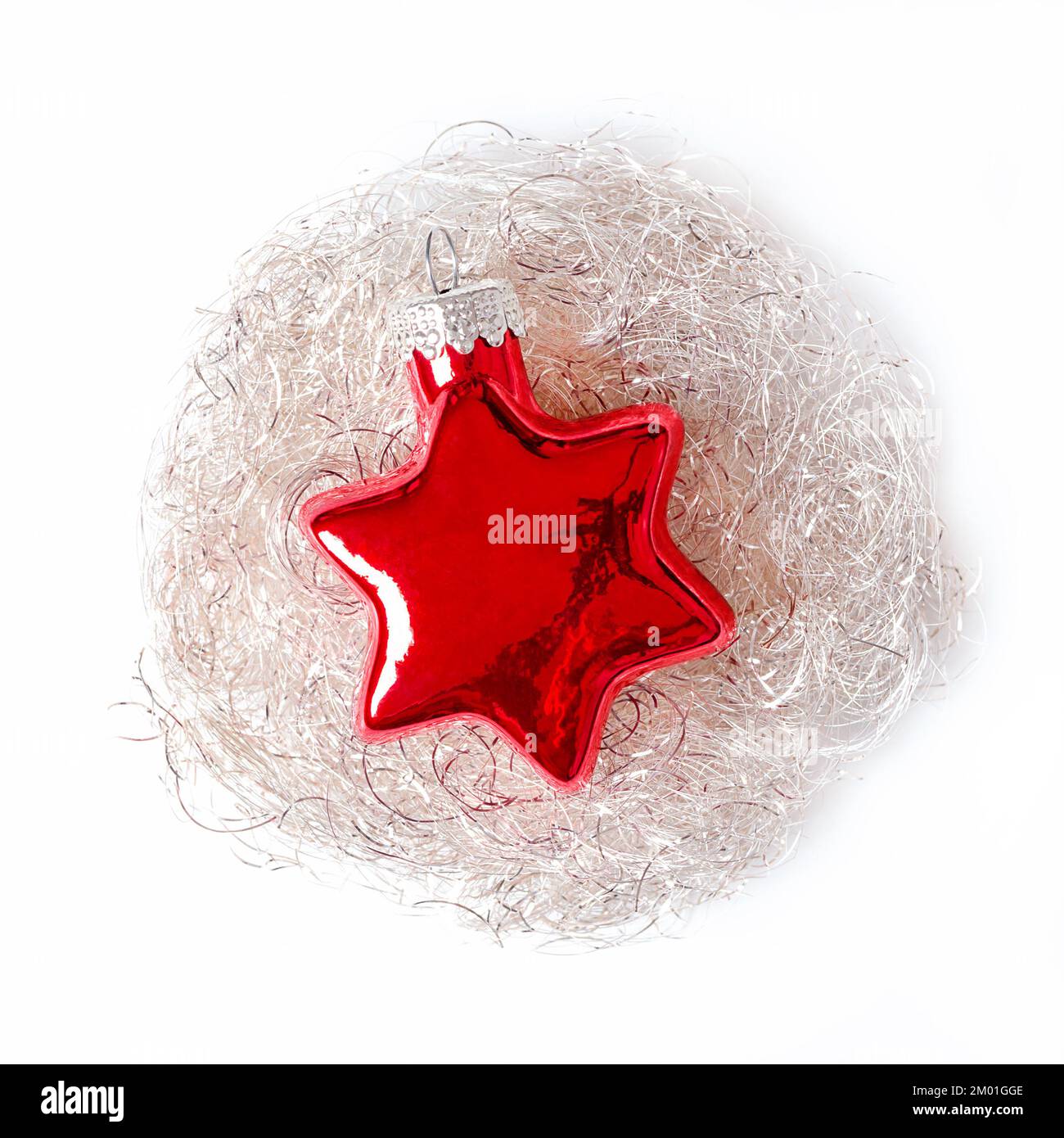 Roter Glasstern, eingebettet in einem silberfarbenen, weißen Engelsnest, auf weißem Hintergrund. Eine sternförmige Glaskugel, die man an einen Weihnachtsbaum hängen kann. Stockfoto