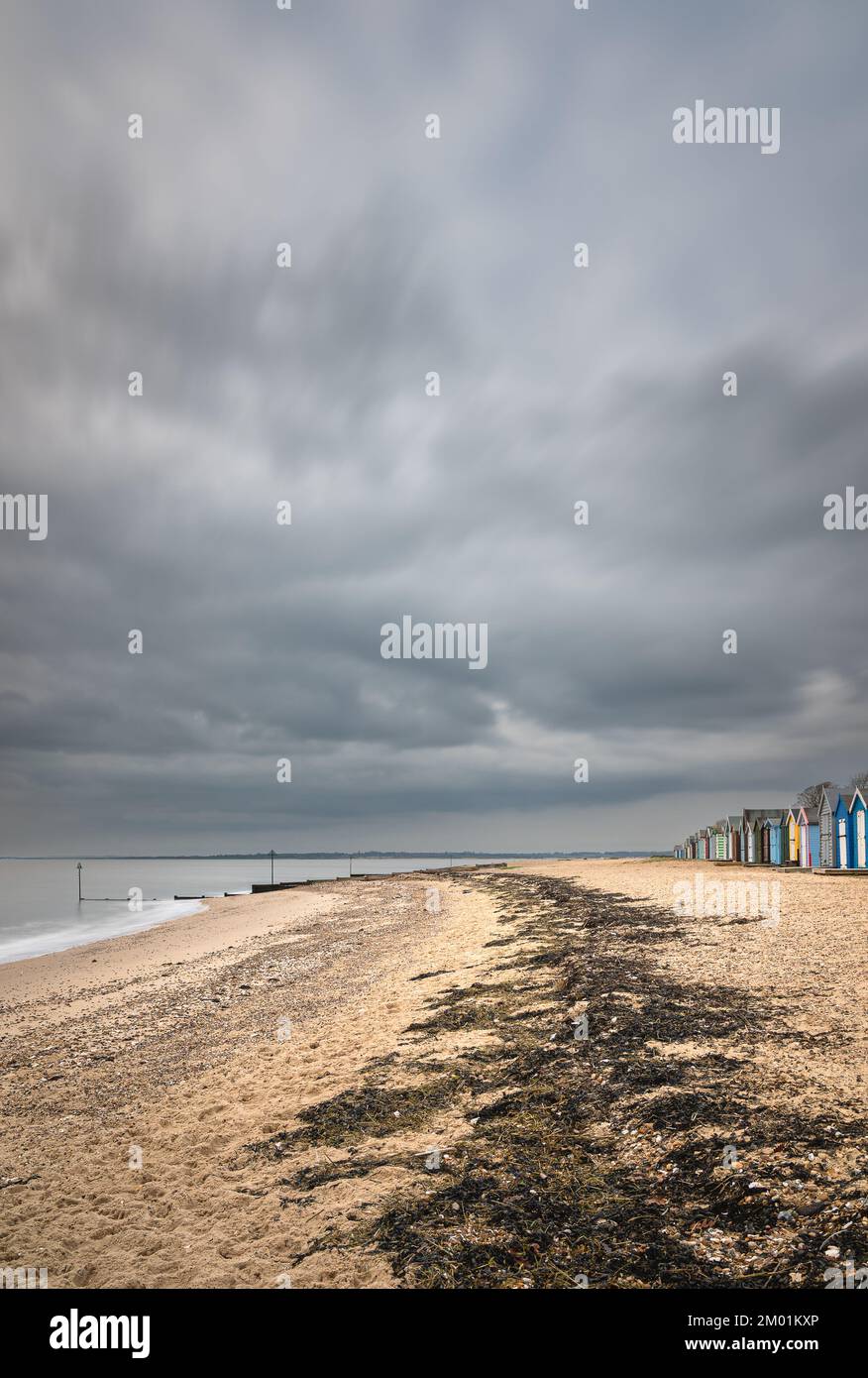 Strandhütten auf Mersea Island in Essex. Moody, bewölkter Himmel und Langzeitaufnahme. Stockfoto