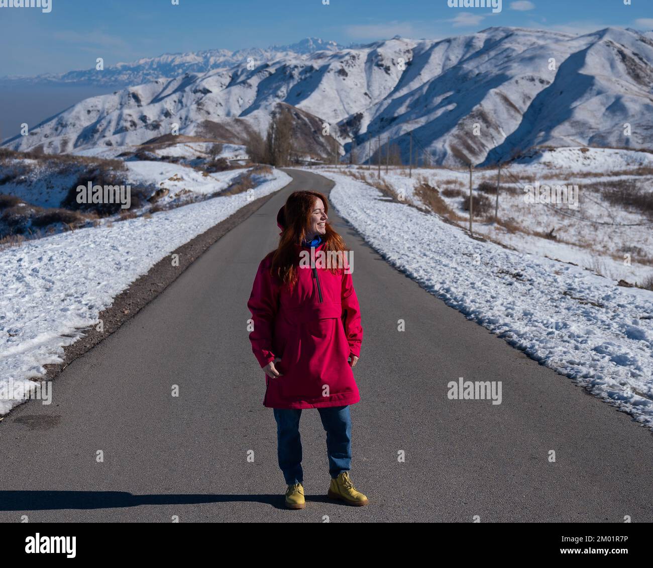 Rothaarige kaukasische Frau in fuchsienfarbenen Jacken in verschneiten Bergen. Stockfoto