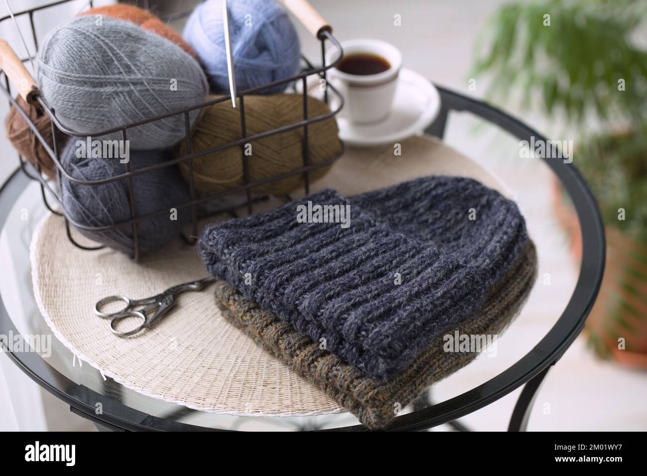 Gestrickte Hüte und Strähne aus Wolle in einem Korb auf einem Tisch Stockfoto