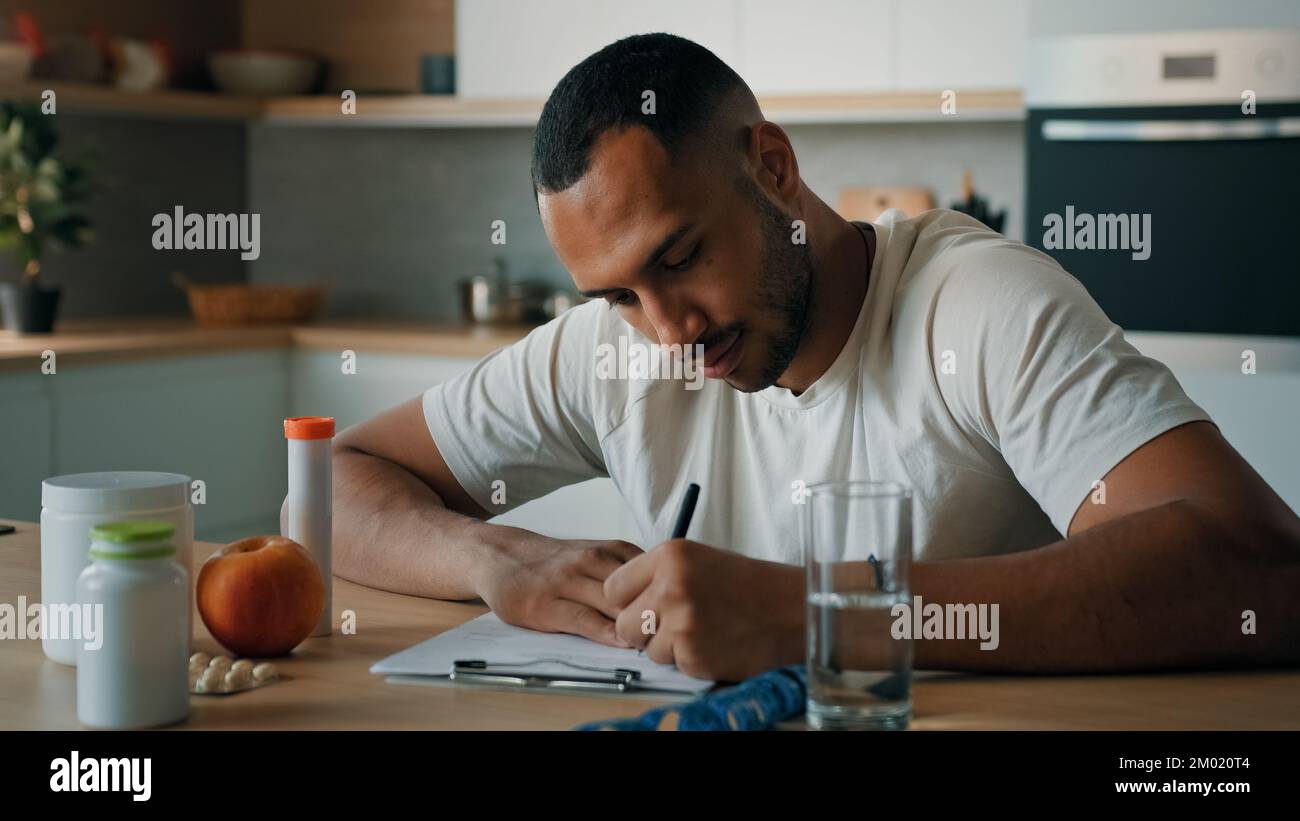 Afroamerikanischer männlicher Ernährungswissenschaftler Mann Sport-Yoga-Trainer sitzt in der Küche und schreibt Rezept gesunde Ernährung Fitness-Diät auf Papier Stockfoto