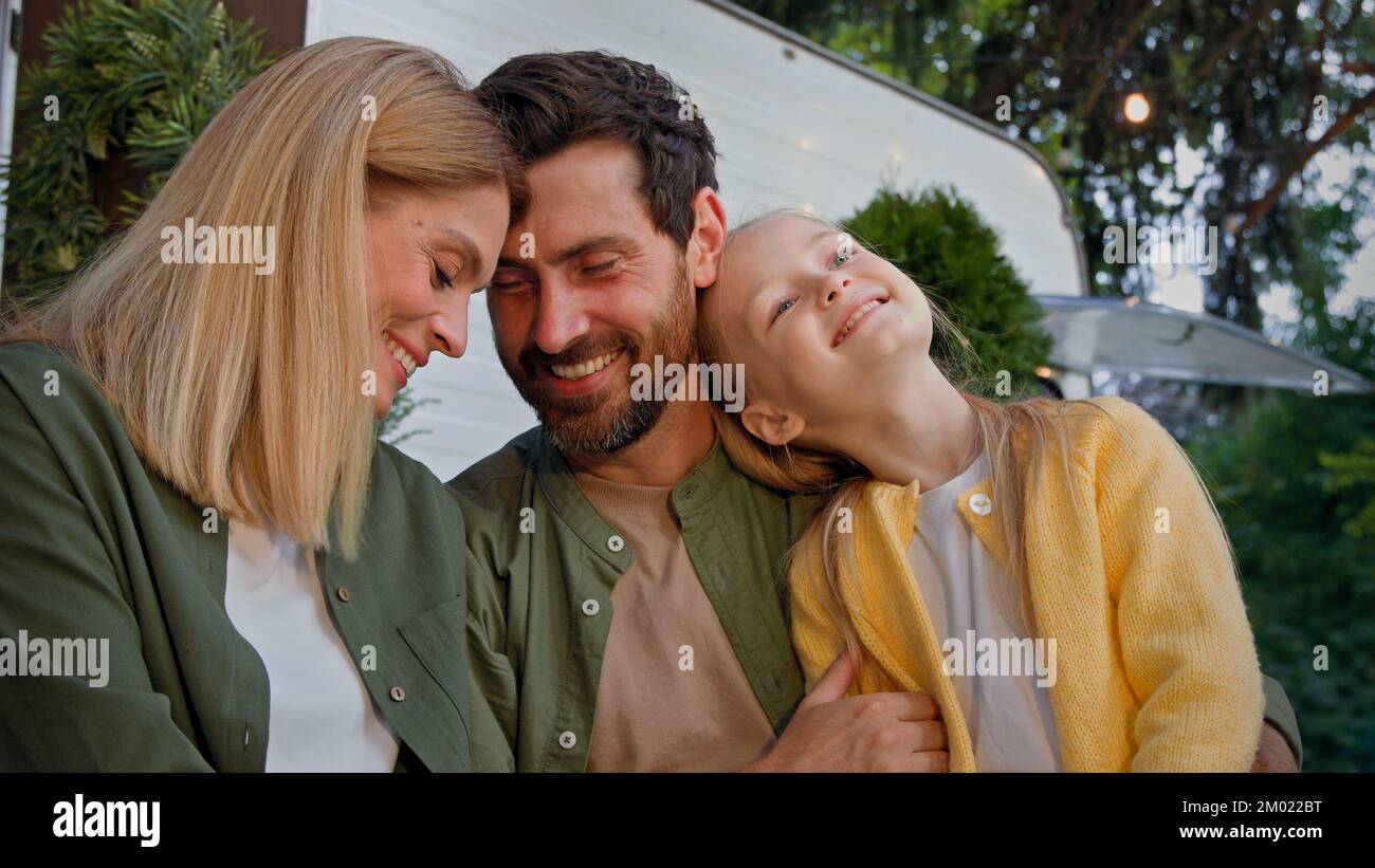 Kaukasische glücklich liebende Familie im Freien reden Papa berühren Nase von kleinen Tochter Kind Mädchen und Mutter Frau küssen bärtigen Vater auf Wange Umarmung Stockfoto