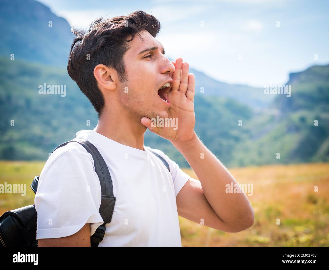 Männlicher Wanderer ruft in den Bergen mit der Hand am Mund an Stockfoto