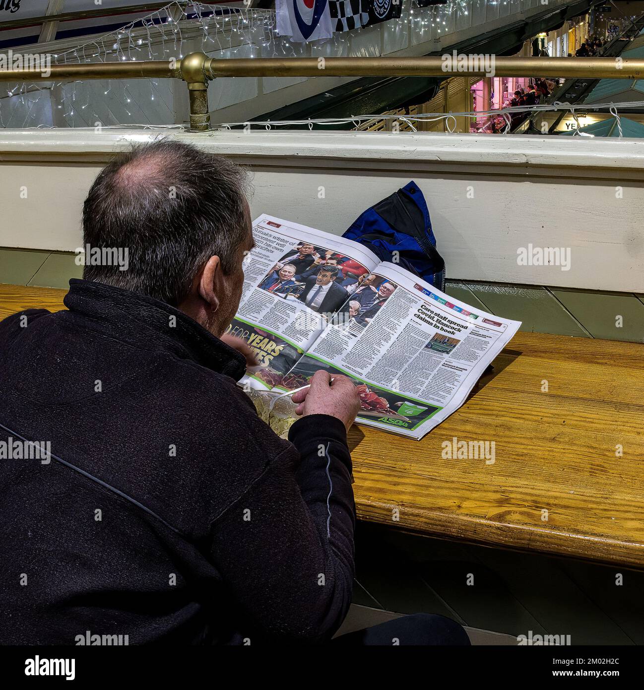 Ein Mann liest eine Zeitung, während er eine Schüssel Suppe im Cardiff Indoor Market isst. Klare Aufnahme des Artikels über PM Sunak. Stockfoto