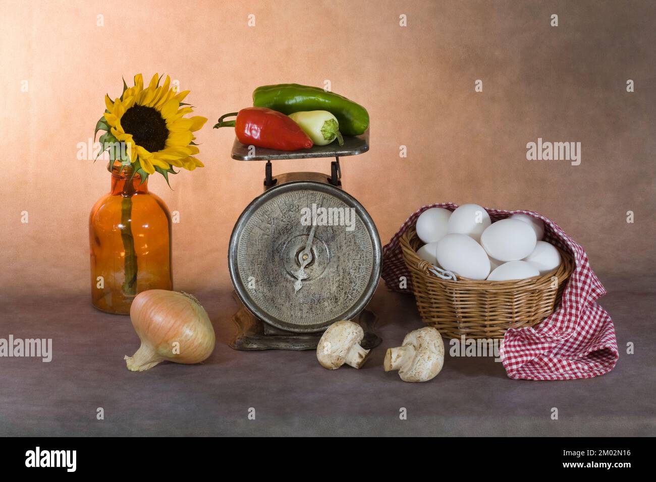 Ein Kunstfoto von einem Dutzend Eiern in einem Korb, Gemüse in einer alten Größe und eine Sonnenblume in einer alten Flasche. Stockfoto