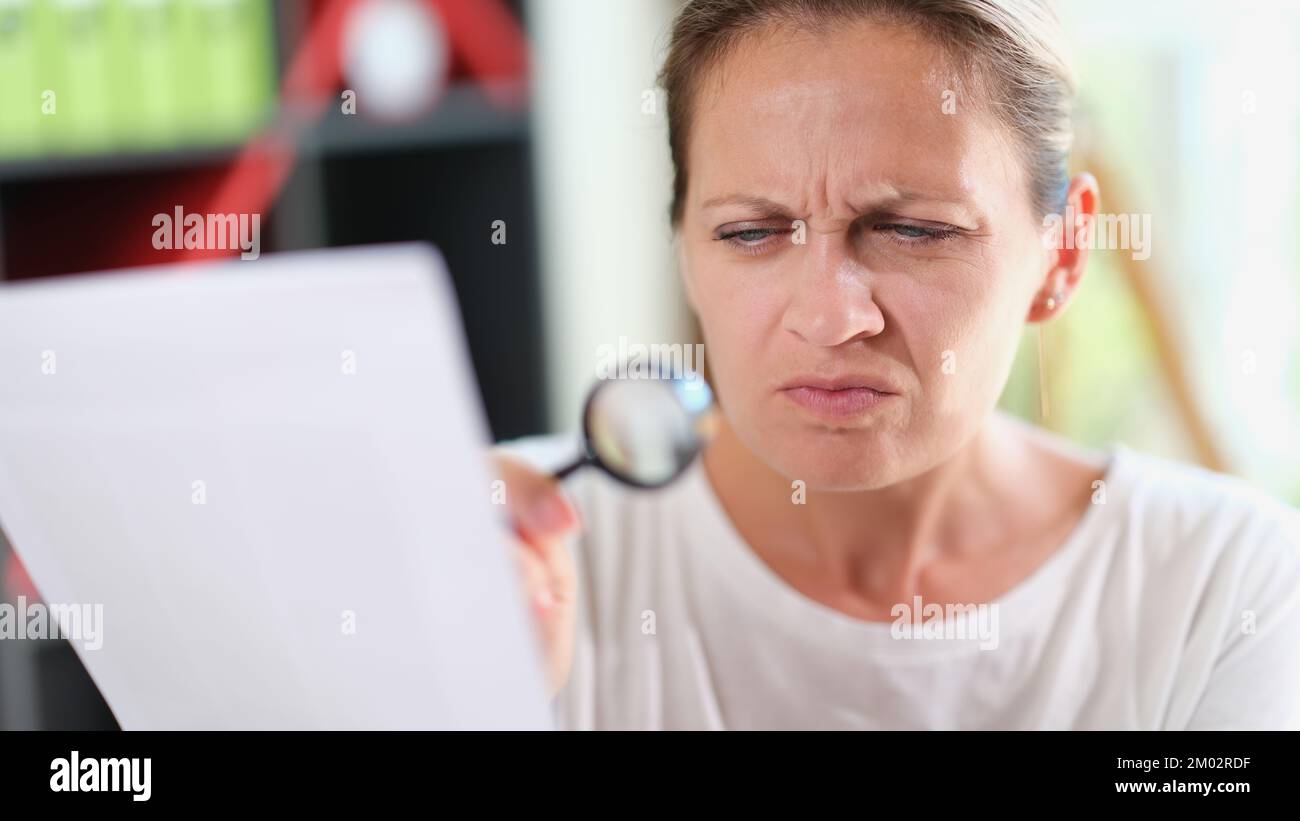 Eine Frau mit verwirrtem Gesicht liest Dokumente oder Rezepte mit einer Lupe in der Hand. Stockfoto