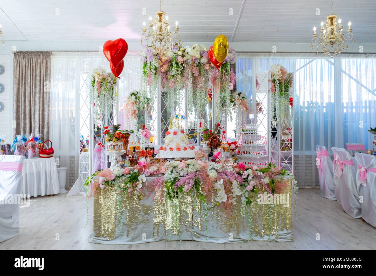 Ein großer Kuchen auf dem Tisch der Braut. Der Hochzeitstisch der Braut und des Bräutigams ist mit vielen verschiedenen Blumen dekoriert Stockfoto