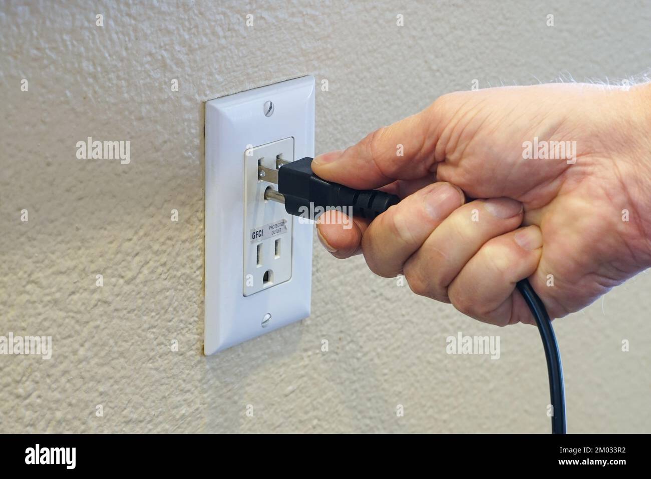 Die Hand eines Mannes, der das Netzkabel an die Stromversorgung anschließt Stockfoto