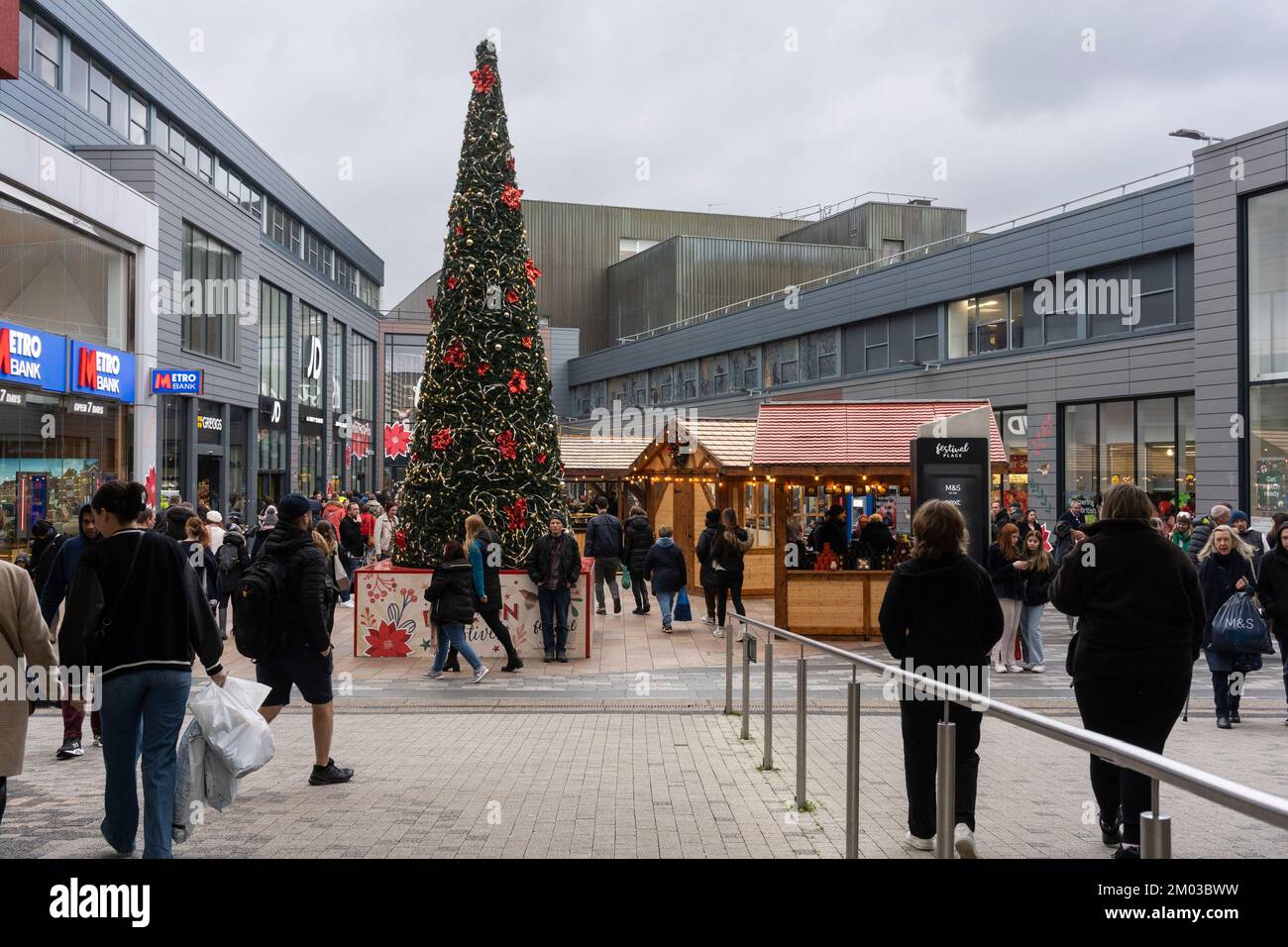 Weihnachtsfeiern im Einkaufszentrum Malls mit einem großen dekorierten Weihnachtsbaum und einem Weihnachtsmarkt mit Holzkabinen. Basingstoke, Großbritannien Stockfoto