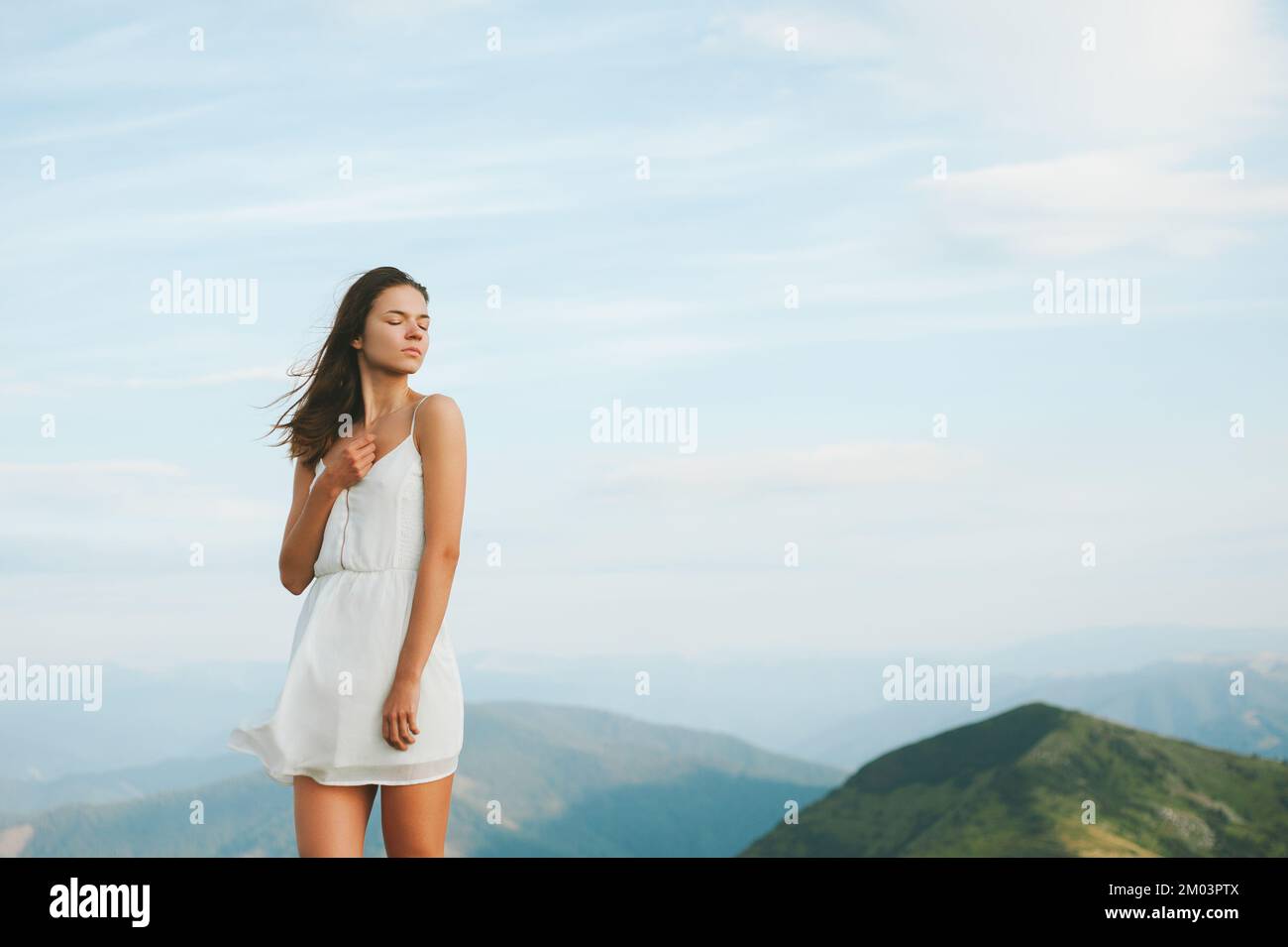 Fröhliche lächelnde junge Frauen in weißem Kleid, die auf dem Berg ein weißes Kleid präsentieren, auf dem Berg gegen den Wolken stehen, Foto aufgenommen in den Karpaten Stockfoto