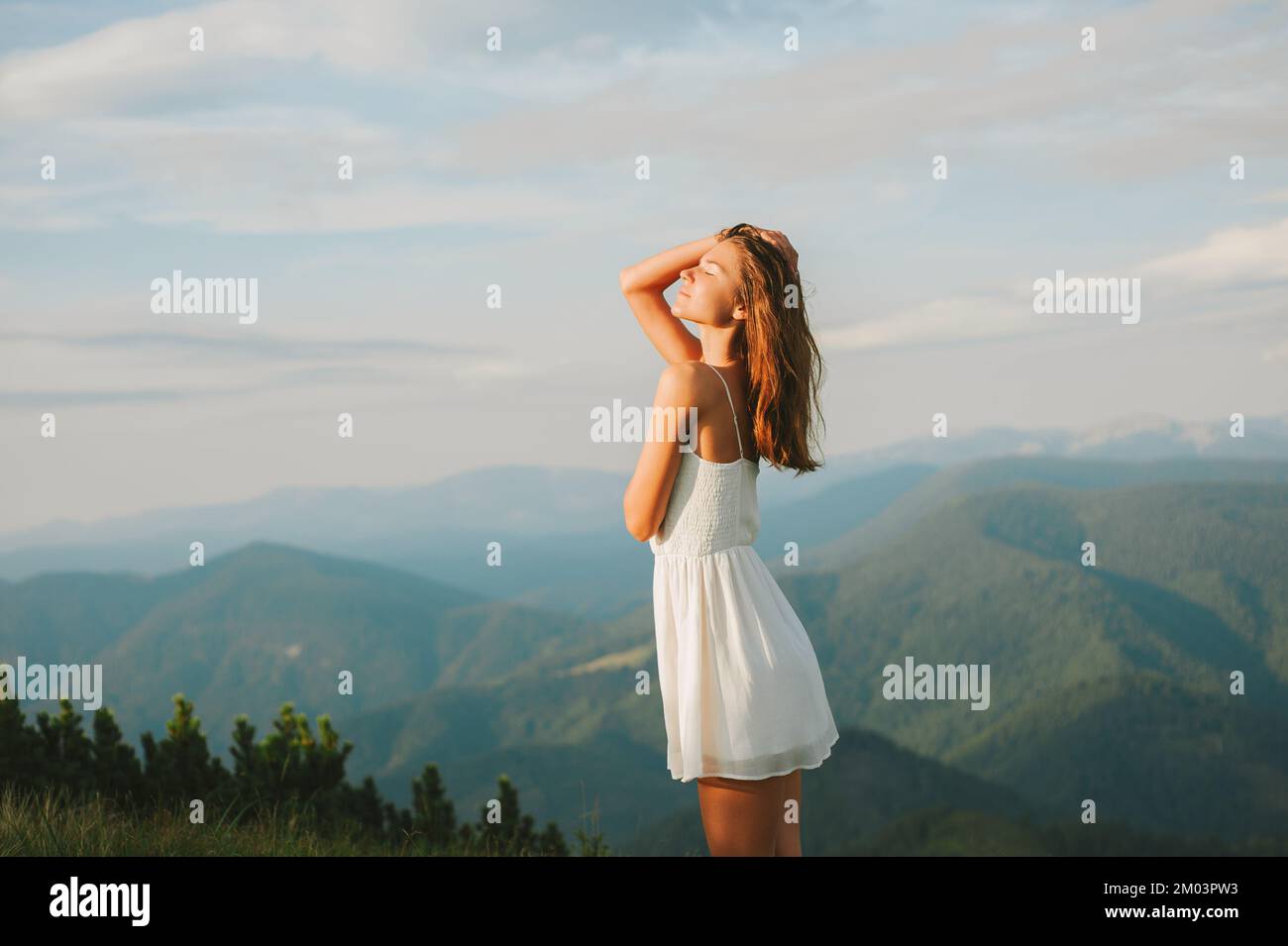 Fröhliche lächelnde junge Frauen in weißem Kleid, die auf dem Berg ein weißes Kleid präsentieren, auf dem Berg gegen den Wolken stehen, Foto aufgenommen in den Karpaten Stockfoto