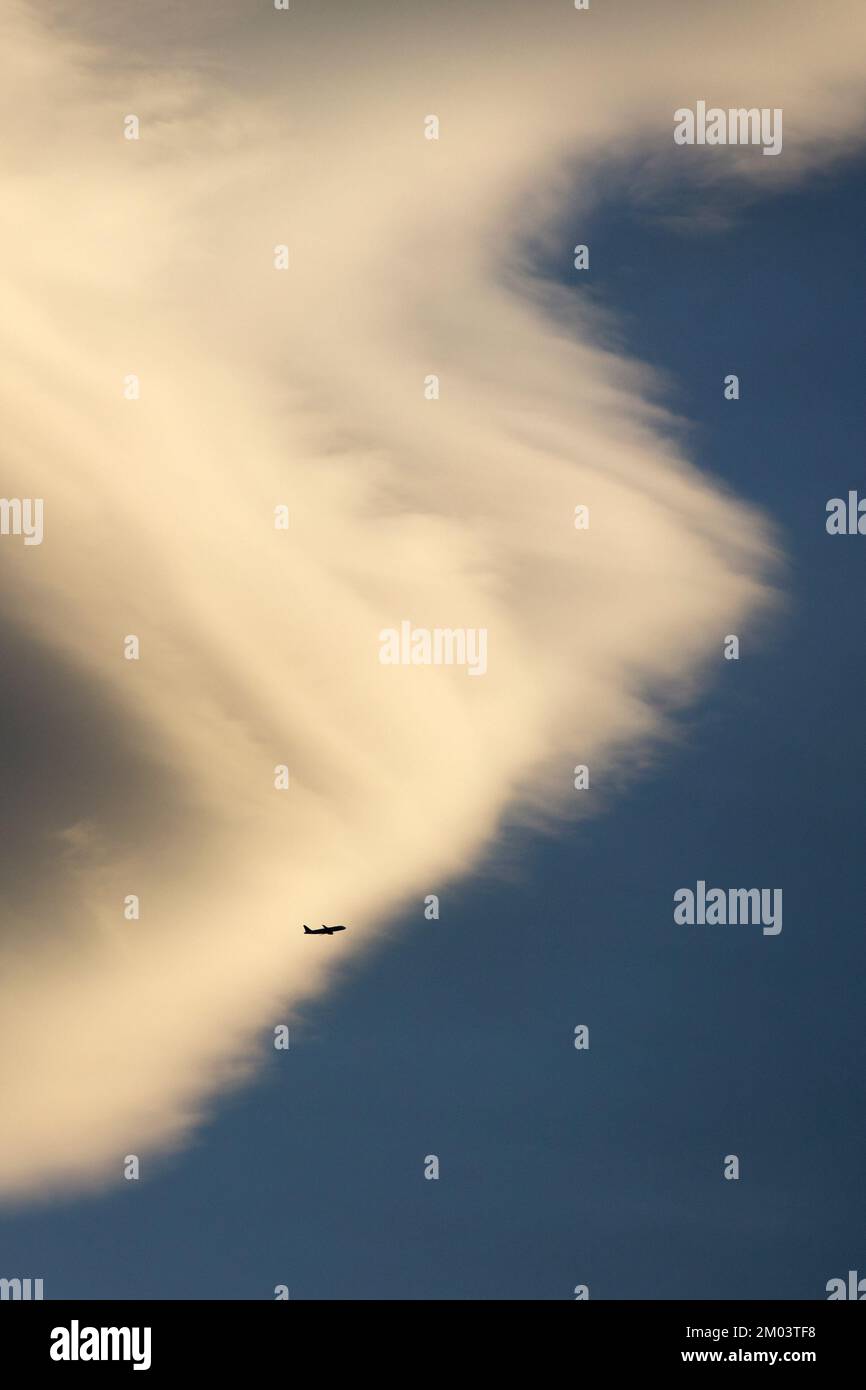 Flugzeug im Flug Silhouette gegen riesige weiße, flauschige Wolke am blauen Himmel. Stockfoto