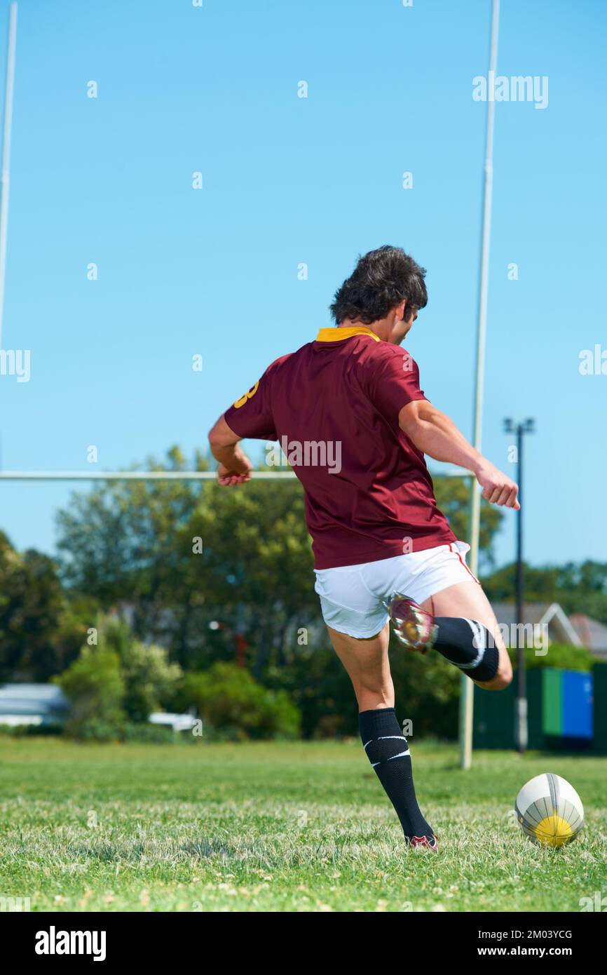 Treten, um zu gewinnen. Rückansicht eines Rugbyspielers, der auf dem Rugbyfeld einen Ball tritt. Stockfoto