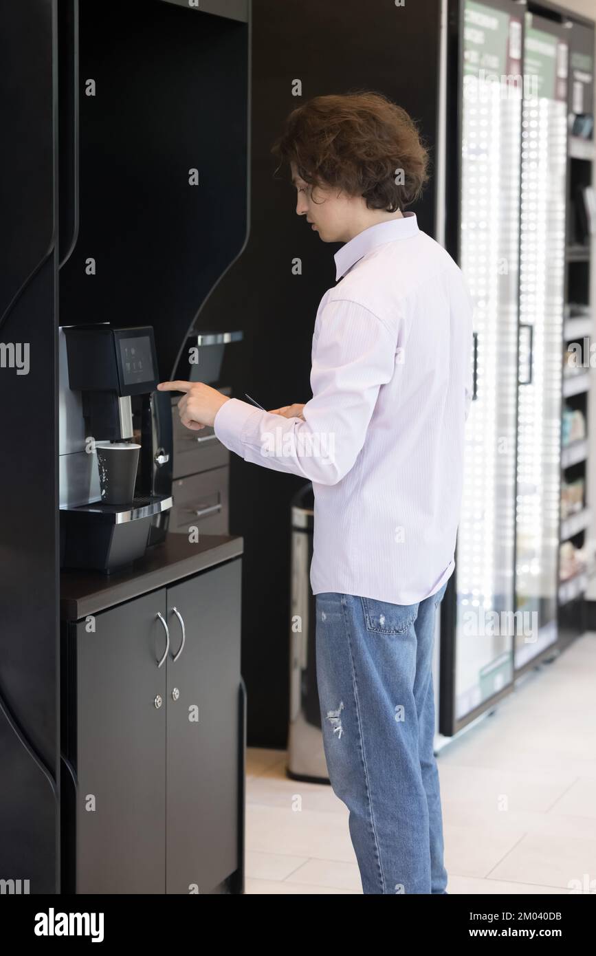 Junger Mann bereitet Kaffee mit einem professionellen Verkaufsautomaten zu Stockfoto
