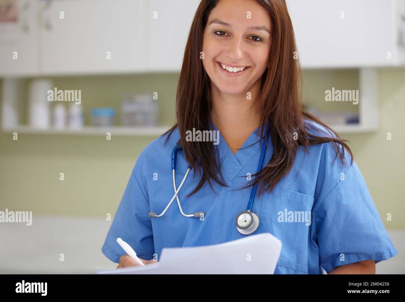 Medizin ist mein Leben. Eine entspannte Frau in Kittel, die Dokumente hält und die Kamera anlächelt. Stockfoto