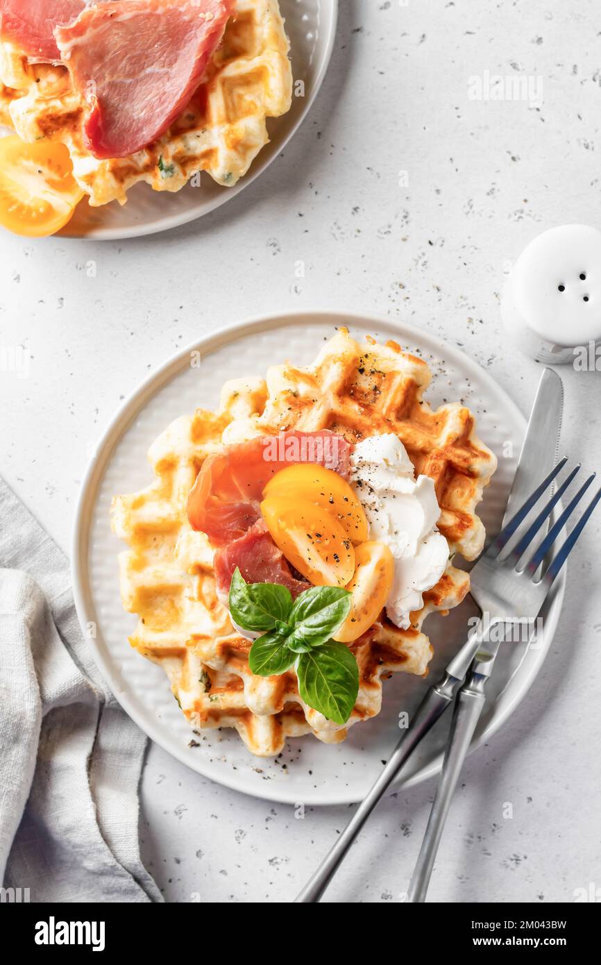 Käse- oder Kartoffelpuffer mit Tomaten, Frischkäse, Schinken und Bazil-Blättern, Besteck und Leinenserviette. Leckeres, herzhaftes Frühstück Stockfoto