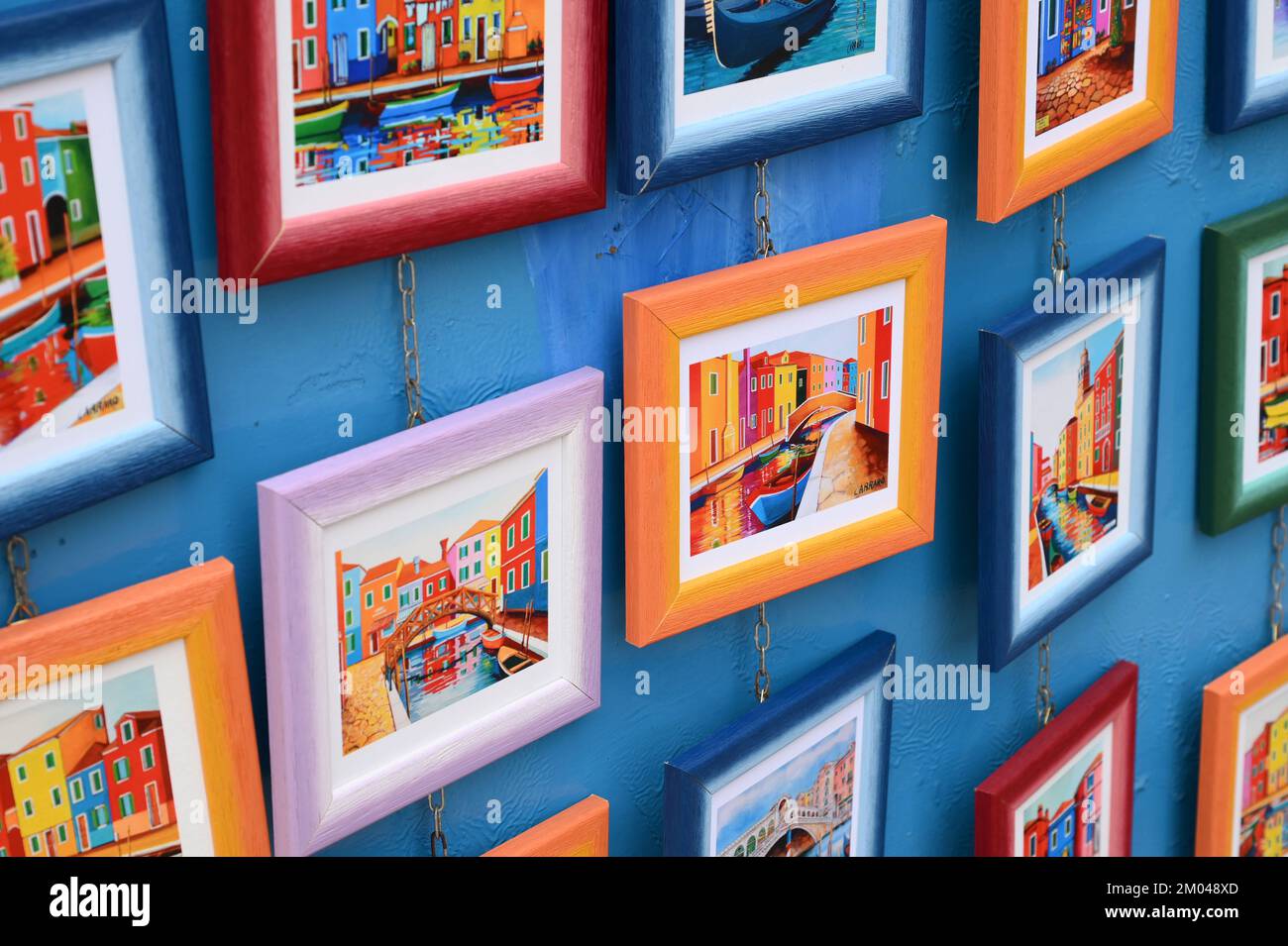 Von oben mehrfarbige Rahmen mit hellen Bildern von Kanälen, die an einer blauen Wand an der Straße der Insel Burano hängen Stockfoto