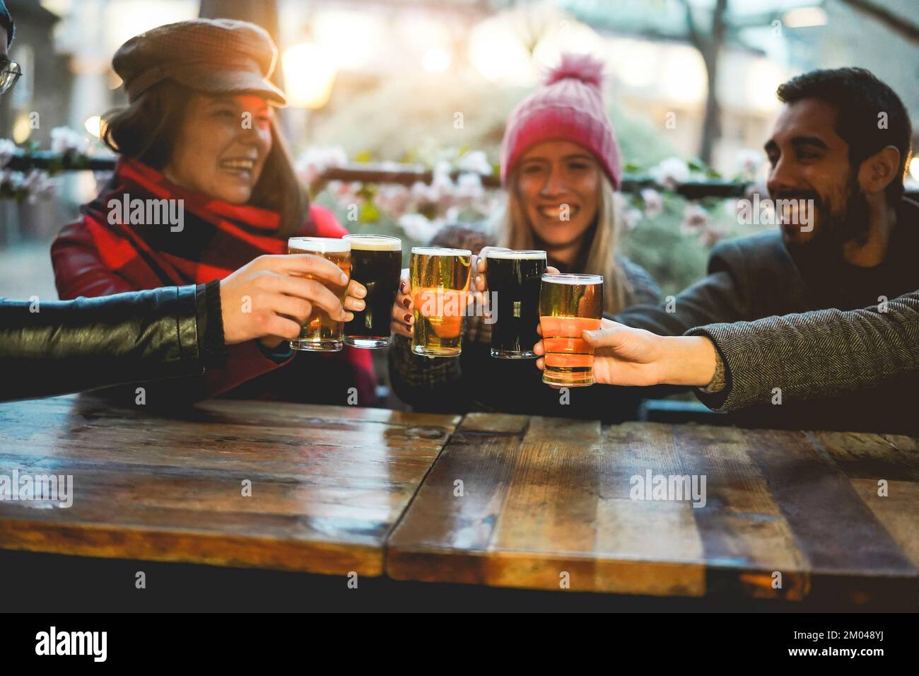 Junge Leute jubeln mit Bier im Pub-Restaurant – weicher Fokus auf die rechte Hand, die Glas hält Stockfoto