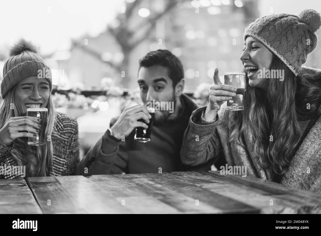 Junge Leute, die Spaß beim Trinken von Bier im Pub-Restaurant haben - weicher Fokus auf den richtigen Mädchenhut - Schwarz-Weiß-Schnitt Stockfoto