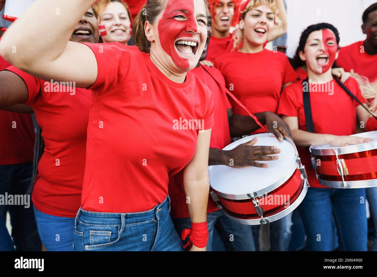 Multirassische rote Sportfans, die beim Unterstützen ihres Teams kreischen - Fußballfans, die Spaß bei Wettkampfveranstaltungen haben - konzentrieren sich auf das Gesicht einer älteren Frau Stockfoto