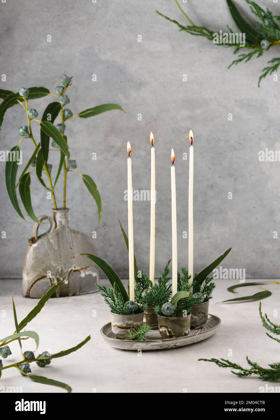 Weihnachtsdekoration mit vier weißen, schmalen Adventskerzen und Eukalyptusblättern. Handgefertigte Inneneinrichtung. Selektiver Fokus. (Eukalyptus globulus) Stockfoto