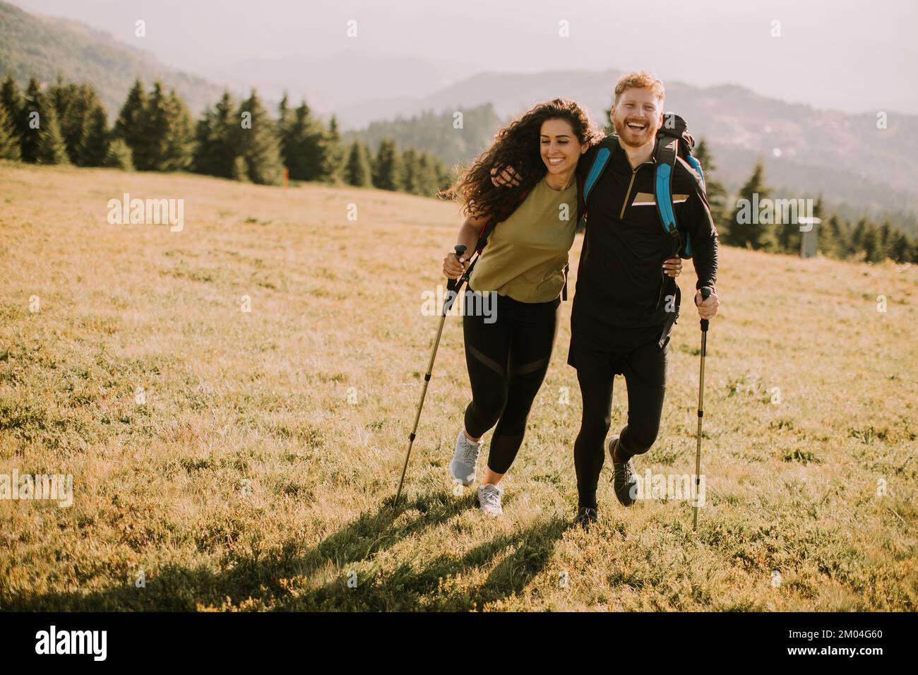 Lächelndes junges Paar, das mit Rucksäcken über grüne Hügel geht Stockfoto