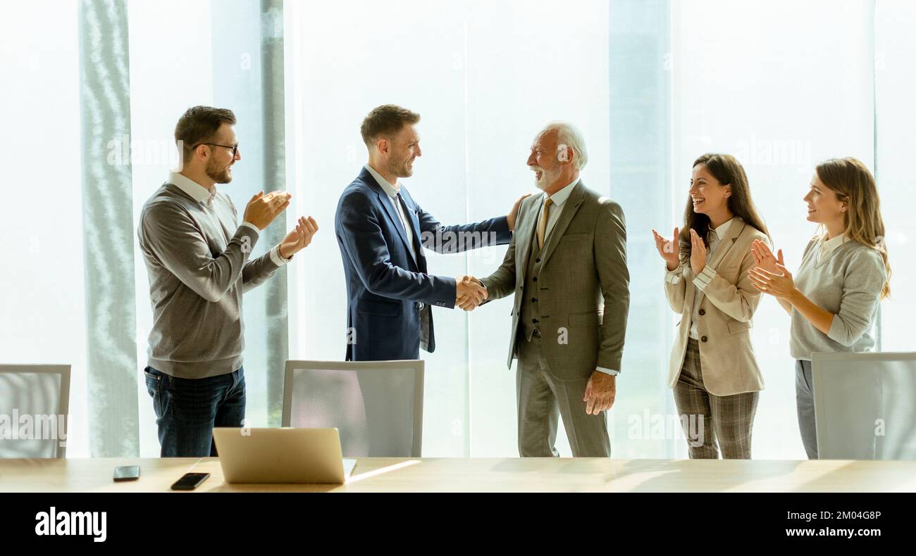 Geschäftspartner schütteln sich im Büro die Hand, nachdem sie mit Mitarbeitern in der Nähe eine Vereinbarung getroffen haben Stockfoto