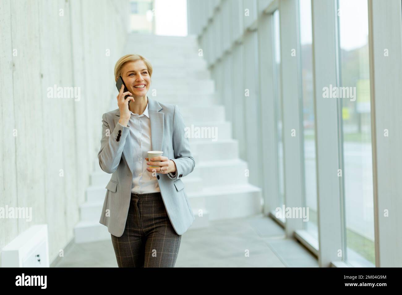 Eine Geschäftsfrau, die ihr Handy benutzt, während sie auf dem modernen Büroflur spaziert Stockfoto