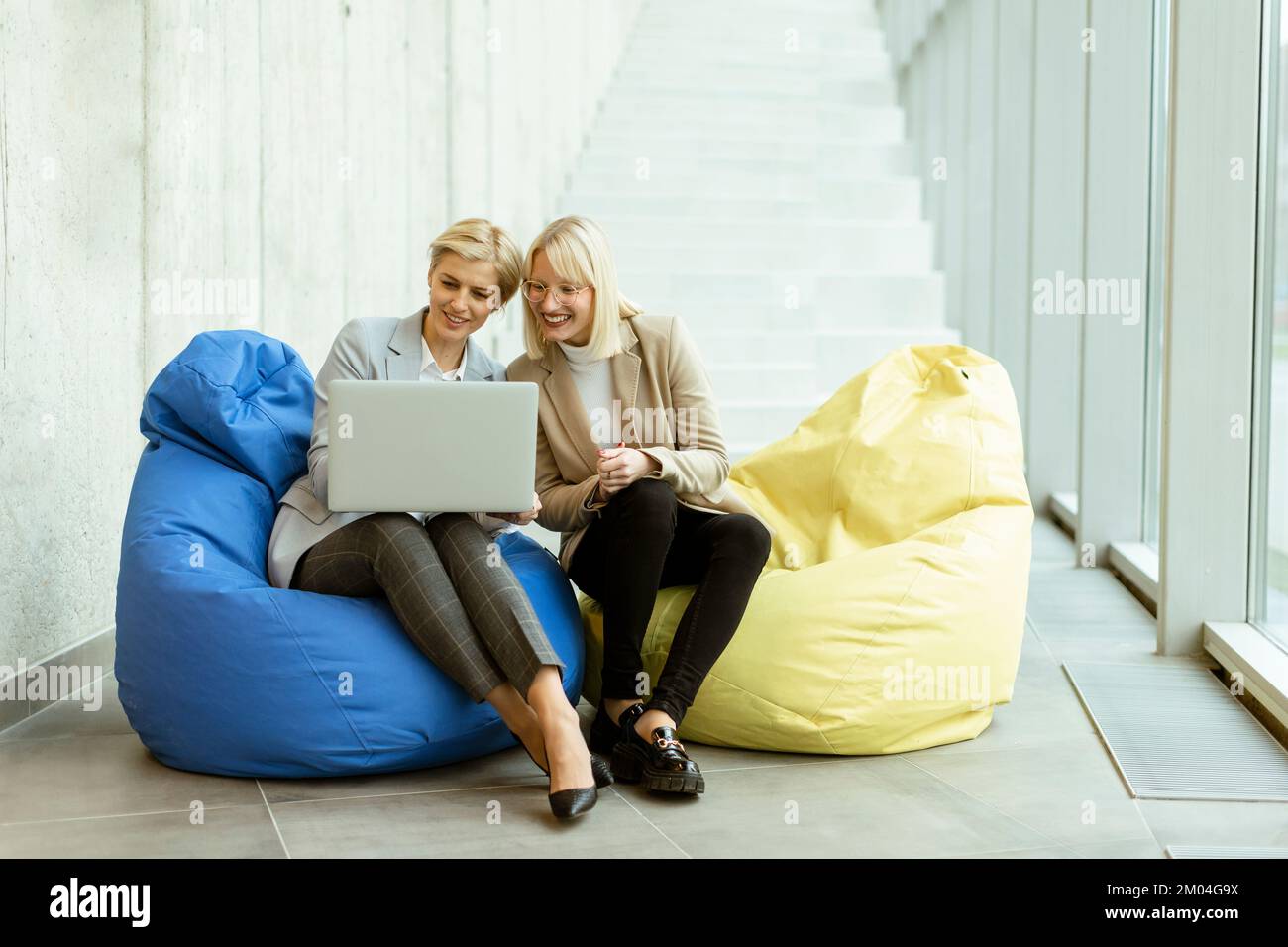 Zwei Geschäftsfrauen, die in einem modernen Büro an einem Laptop mit faulen Taschen arbeiten Stockfoto