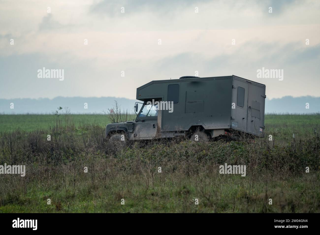Britisches Militär Land Rover Defender Wolf Medizinische Hilfe Leichtes Nutzfahrzeug, das sich auf einer Schlammstrecke auf einer Militärübung, Wiltshire UK, bewegt Stockfoto