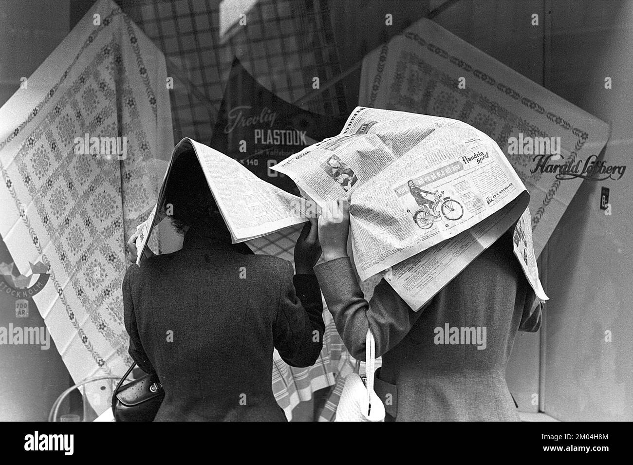 Regenschirme in den 1950er Jahren. Der Regen strömt in Strömen und zwei Damen halten die Tageszeitungen über sich, da sie keinen Schirm haben. Es ist ein Regentag in Stockholm Schweden 1953. ref. 1,2 Stockfoto