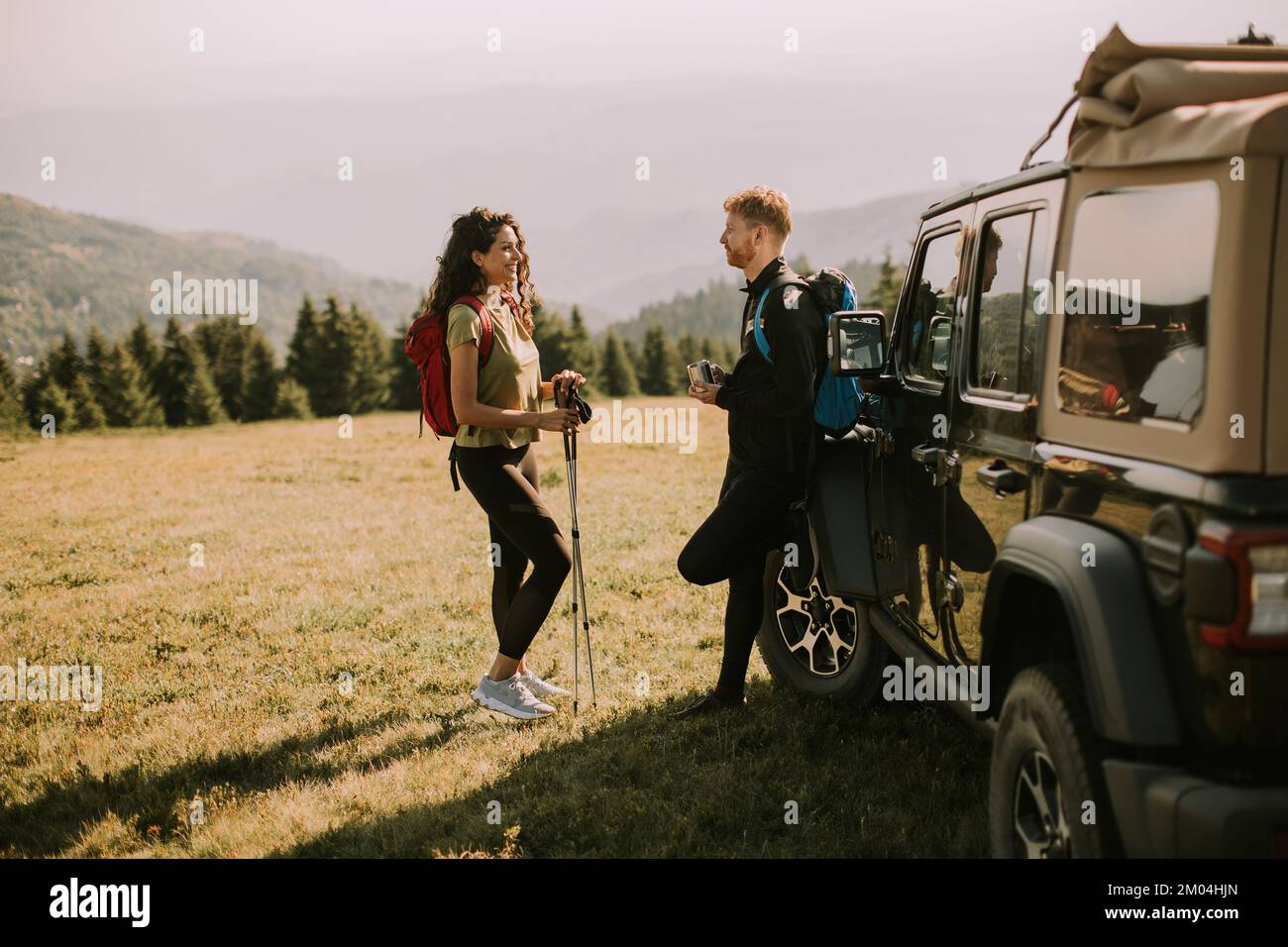 Lächelndes junges Paar bereitet Wanderabenteuer mit Rucksäcken von Geländewagen vor Stockfoto