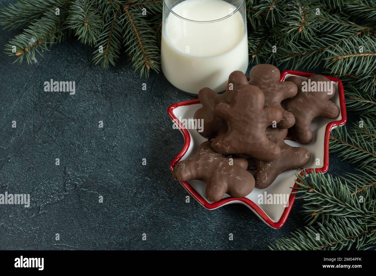 Schokoladen-Lebkuchen-Mann, Weihnachtskekse, ein Glas Milch für den Weihnachtsmann und Baumzweige. Weihnachtszeit Winterkomposition mit Kopierbereich. Stockfoto