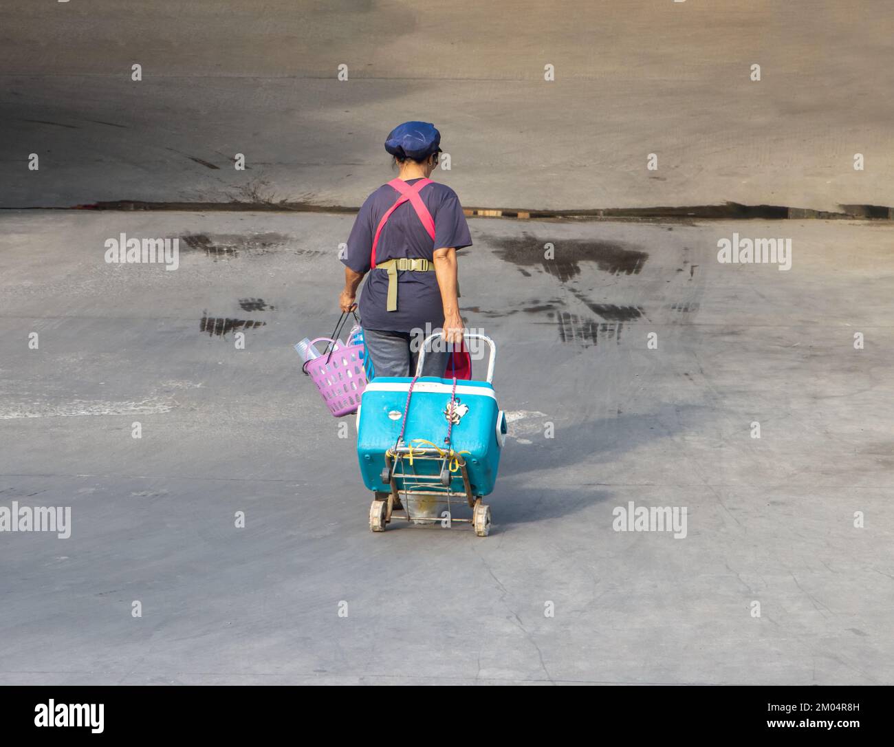 SAMUT PRAKAN, THAILAND, Okt 19 2022, eine alte Frau mit Schürze zieht einen Wagen mit einer Kühlbox auf einer leeren Straße Stockfoto