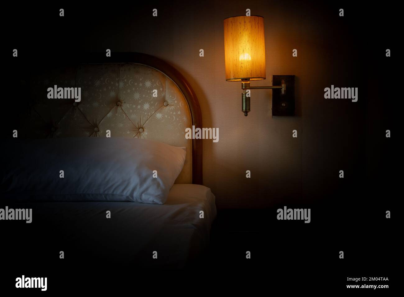 Ein Bett mit einer beleuchteten Lampe, die über dem Nachttisch hängt Stockfoto