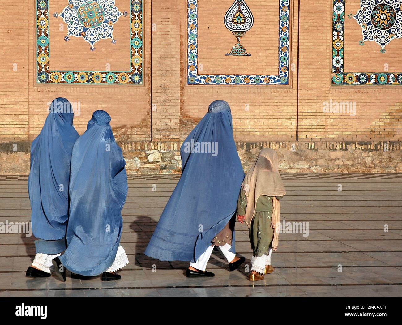Herat im Westen Afghanistans. Die große Moschee von Herat (Freitagsmoschee oder Jama Masjid). Drei Frauen in Burka und ein Mädchen gehen vor die Moschee. Stockfoto