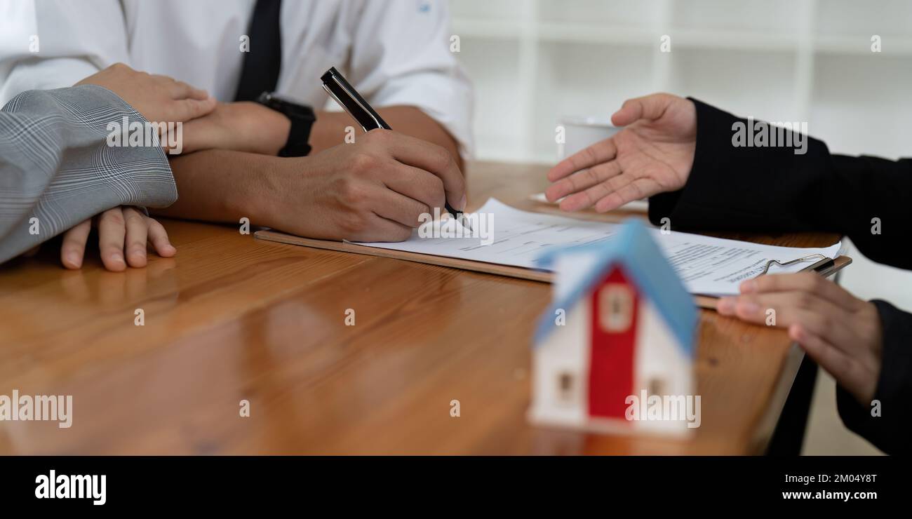 Ein junges Paar unterschreibt einen Vertrag mit einem Immobilienmakler. Stockfoto