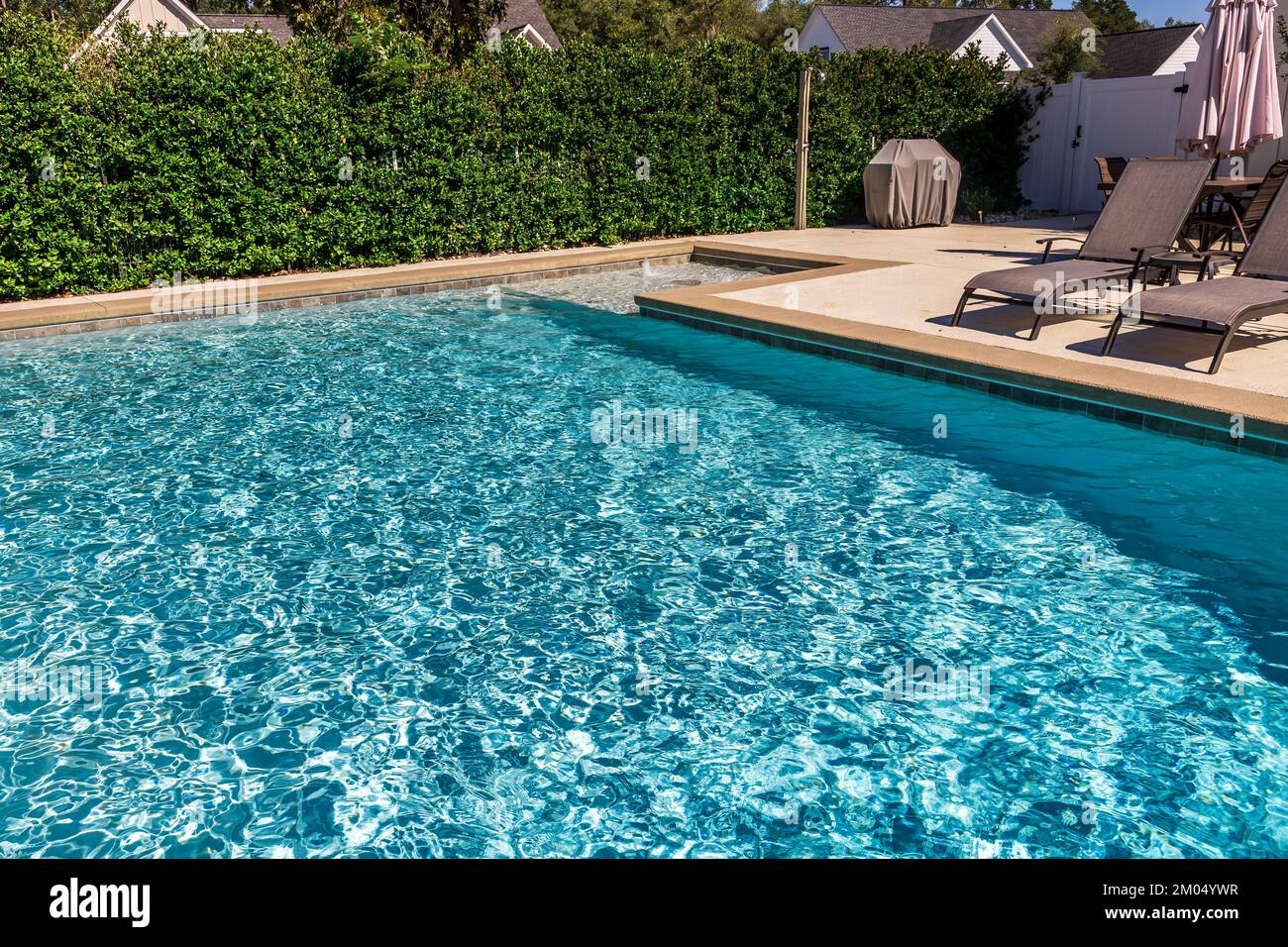 Ein rechteckiger neuer Swimmingpool mit hellbraunen Betonkanten im eingezäunten Garten eines neuen Bauhauses Stockfoto