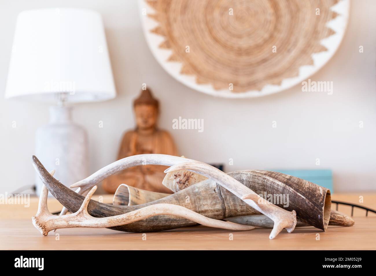 Innenelemente im ethnischen Stil mit Kornukopien in der Mitte des Esstisches, einer hölzernen Buddha-Statue im Hintergrund und einer Korbpflanze in Medit Stockfoto