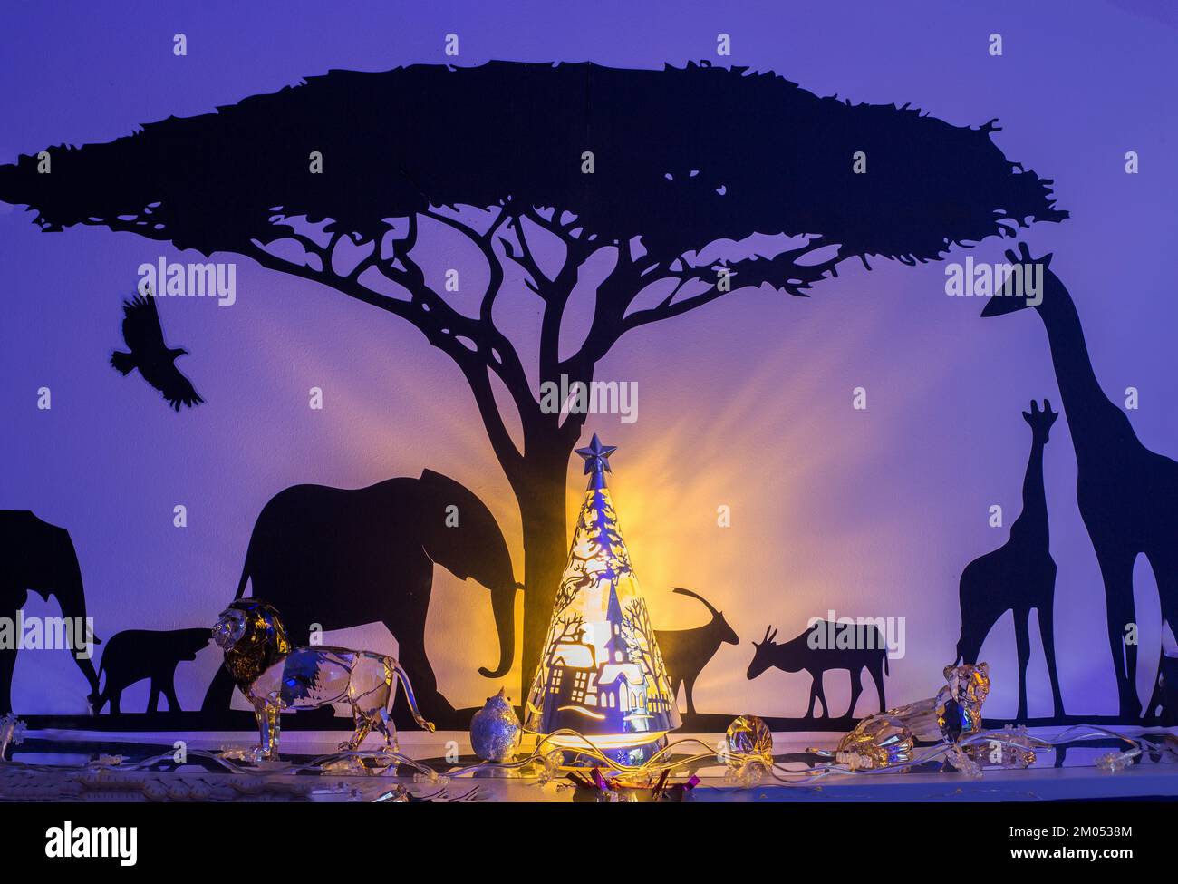 Silhouette einer afrikanischen Weihnachts-Safari-Szene Wanddekor, mit Safaritieren neben einem Akazienbaum und beleuchtetem Weihnachtsbaum. Stockfoto