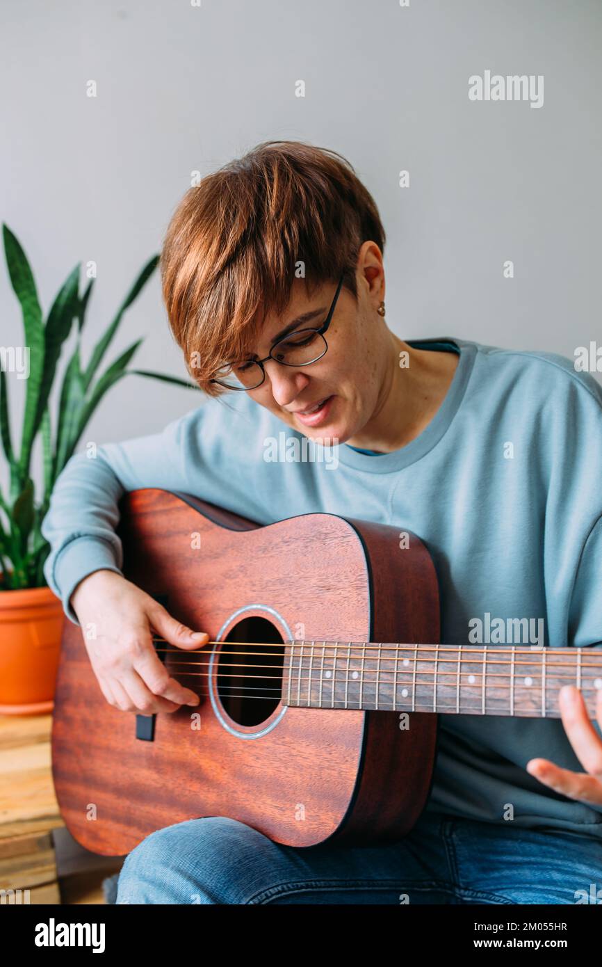 Frau mit kurzen Haaren spielt gerne Gitarre zu Hause. Musikunterricht für Erwachsene Stockfoto