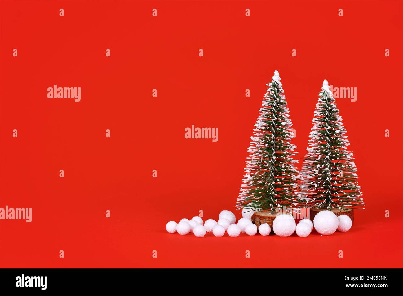 Miniatur-Weihnachtsbäume und Schneebälle auf rotem Hintergrund mit Kopierbereich Stockfoto